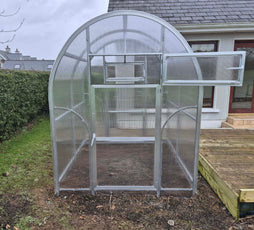 Sigma 200 (Gen III) greenhouse with transparent panels on a grassy area in front of a house.