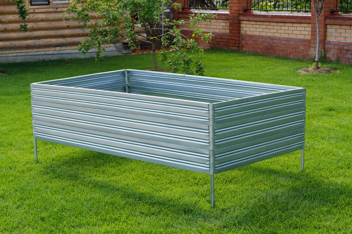A mockup of a metal Planta Garden Bed - 3 Tiers on grass with a wooden fence and trees in the background